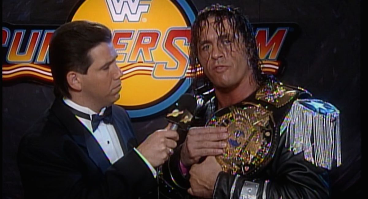 A backstage interview with Bret Hart, with wet hair and classic fringed black jacket, hoists the WWF title over his shoulder.