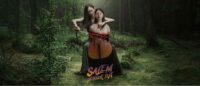 A forest setting where a woman is playing a half person, half cello with a bloody bow