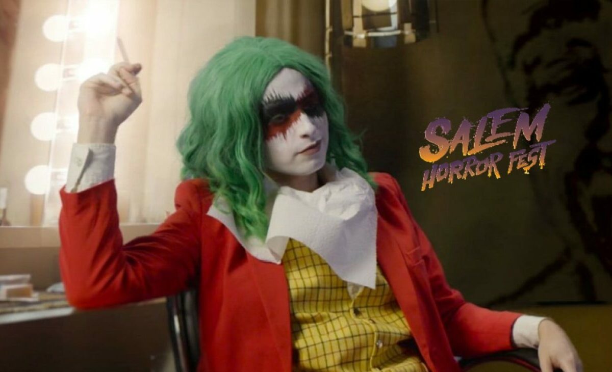 The People's Joker, Joker the Harlequin sits in a chair in a clown outfit and makeup with green hair holding a cigarette in her right hand