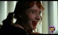 A red-headed womansmiles over her shoulder revealing a mouth full of blood dripping off her teeth and lips in CANNIBAL MUKBANG