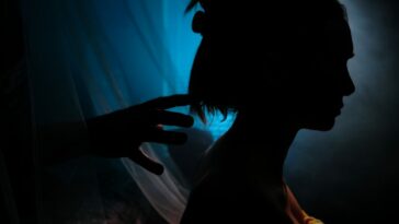 A close up shot of a woman's silhouette in profile as a sinister hand reaches for her head in The People in the Walls.