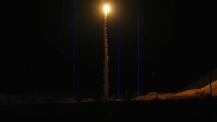 Lasers point up at the sky as a rocket flies through the center 