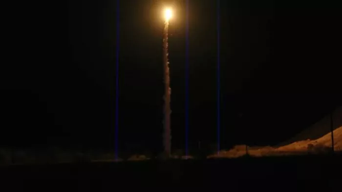 Lasers point up at the sky as a rocket flies through the center