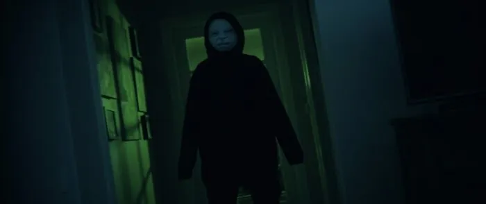 A person in a hallway wearing a grotesque baby mask