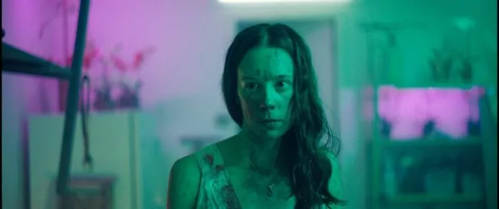 A woman in green and pink lighting covered in blood.