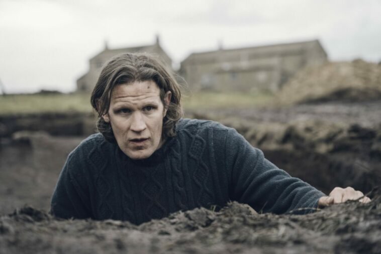 A man in a hole outside, surrounded by soil and looking serious