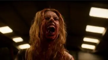 A blonde woman covered in blood sneers to reveal her blood stained teeth