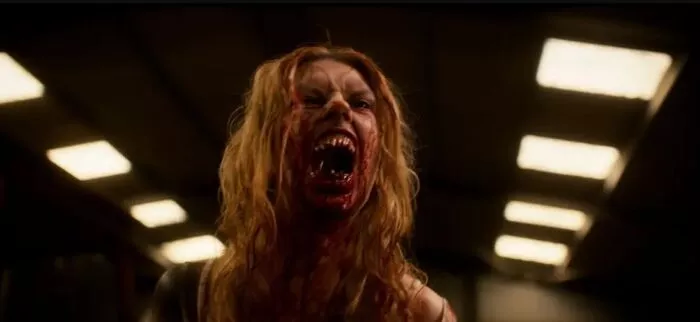 A blonde woman covered in blood sneers to reveal her blood stained teeth