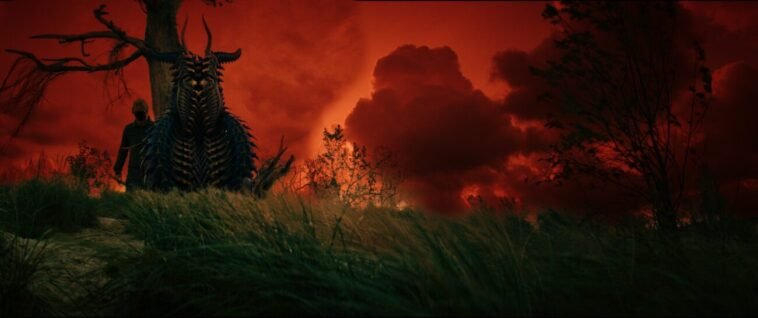 A man standing by a tree next to a strange being under a red skyd