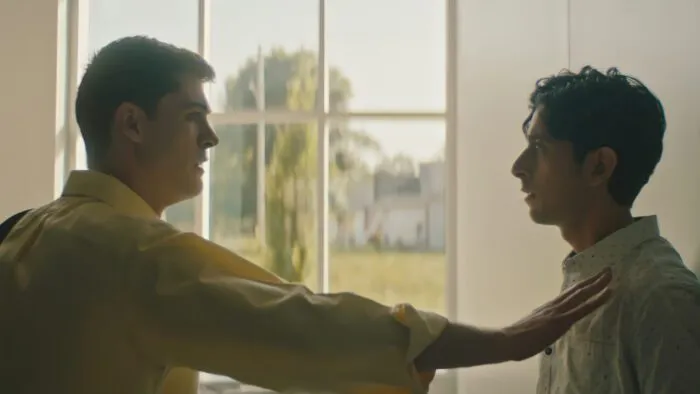 A young man extends his forearm, holding another young man against a wall