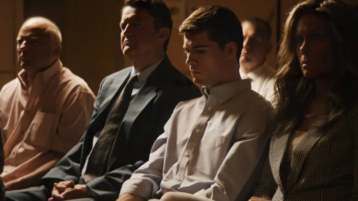 A young man looks pensive surrounding by older people watching something out of frame