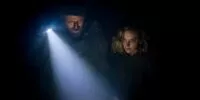 a man holding a flashlight stands beside a woman