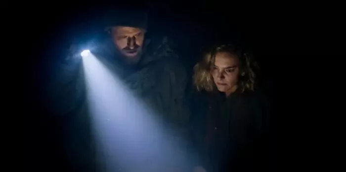 a man holding a flashlight stands beside a woman