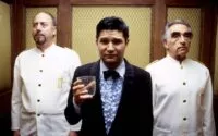 A man holding a glass and two waiters behind him