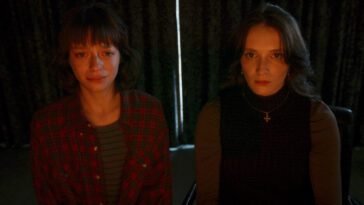 two women behind a drawn curtain, the red glow of a monitor shining off their faces in Red Rooms