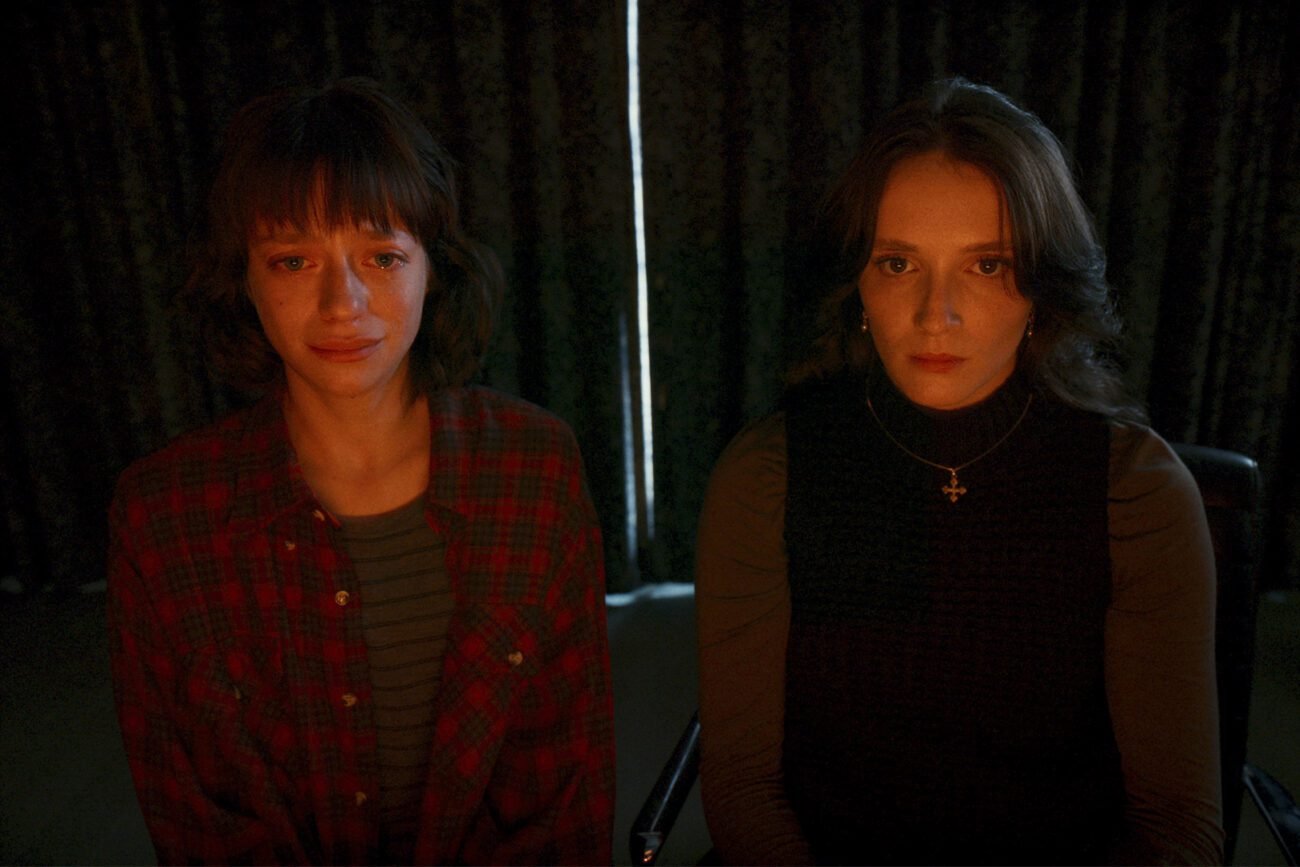two women behind a drawn curtain, the red glow of a monitor shining off their faces in Red Rooms