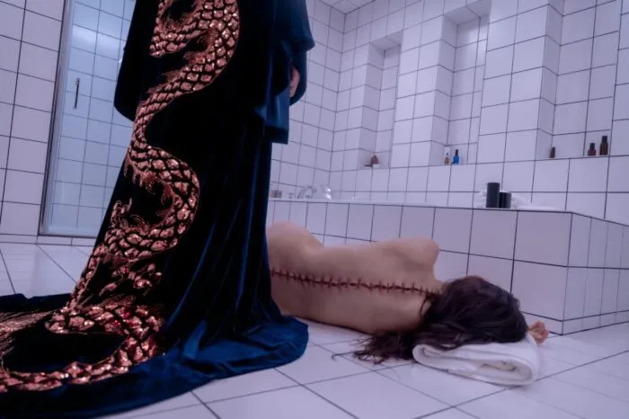 A woman in a robe looking at a body on the floor