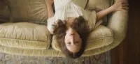 A woman lying upside down on a couch