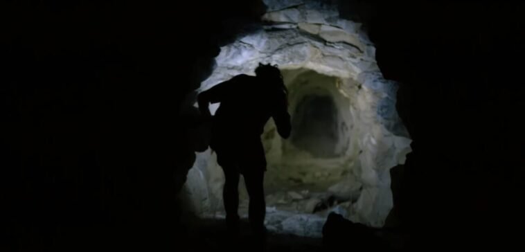 The silhouette of a man standing in the entrance of a cave.