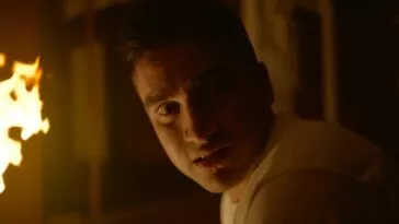 A man looks behind him with fire in the background.