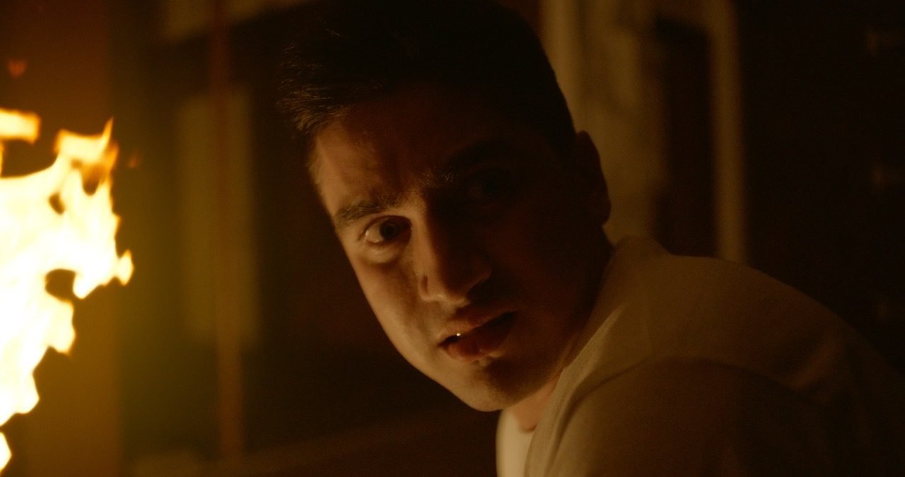 A man looks behind him with fire in the background.
