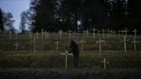 A man pounding a cross into the ground in a field of crosses