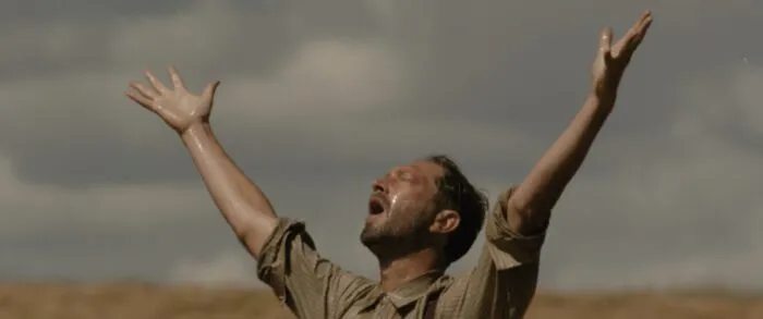 A man in a field raises his arms to the sky as if in prayer.