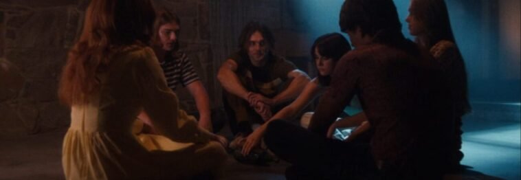 A group of teens sit on the floor playing spin the bottle