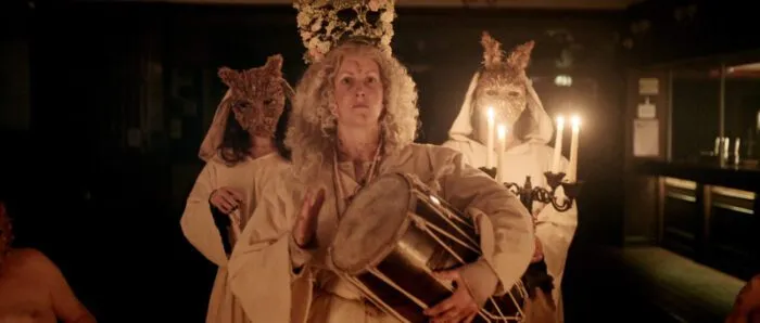 The three members of a coven, two in masks and one with a flower headress holding a drum.