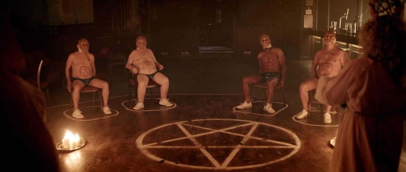 Two men tied to chairs in circles outside of a pentagram contained in a circle.