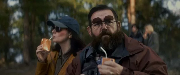 A man and woman drinking juice boxes in the woods.