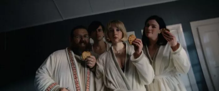 Four people in bathrobes smiling holding cookies.