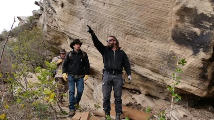 A man points to the sky on a rocky path, two others follow behind
