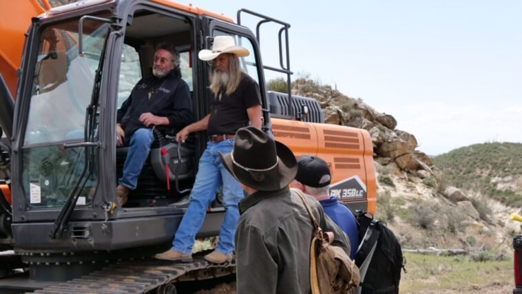 Duane Ollinger sits in excavator, while Charlie Snider, Josh Feldman, and James Keenan gather around Bead Site. // Image Courtesy of Warner Bros. Discovery