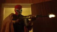 A luchador wrestler stands in a doorway, firing a machine gun