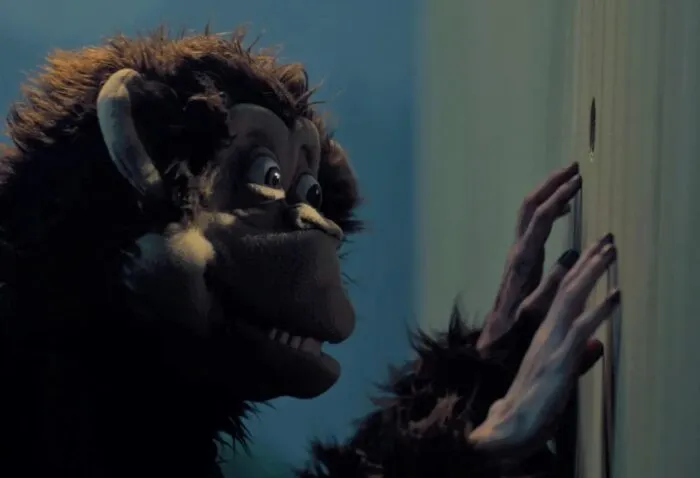 A monkey puppet peeks through a hole in a fence