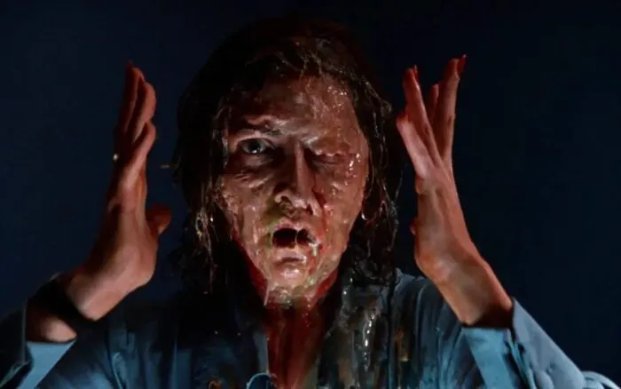 A woman holds her hands up to either side of her head as her face melts off