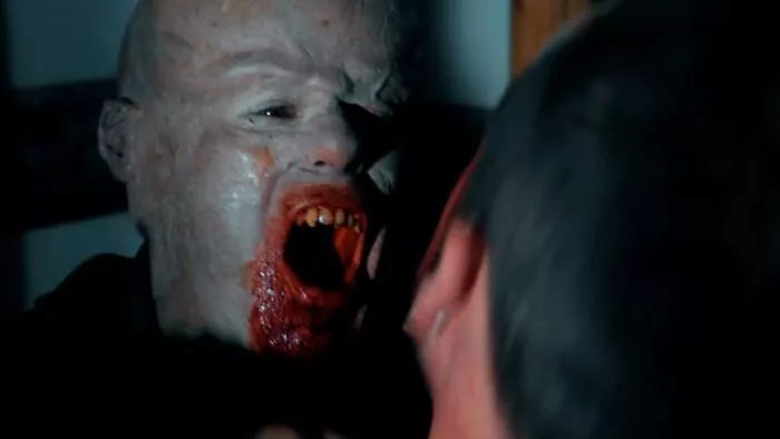 A humanoid being with an abnormally sized head has blood around his mouth as it lunges toward the person facing it in CRYPTIDS