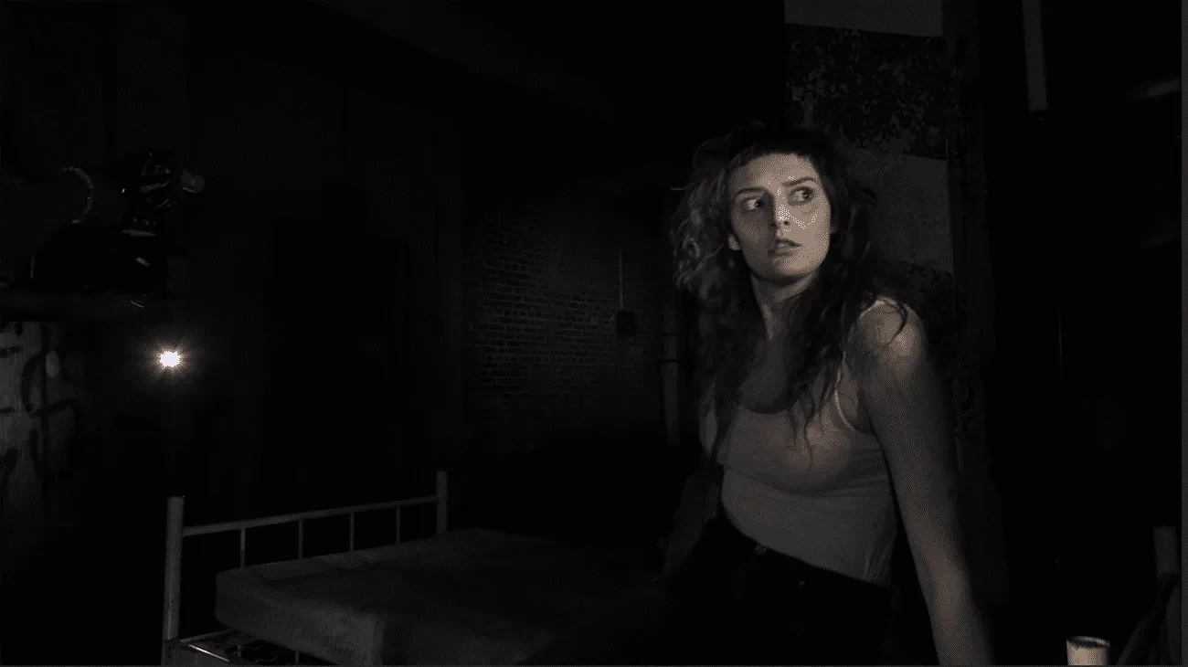 A woman looks scared looking off camera as another camera projects light onto her