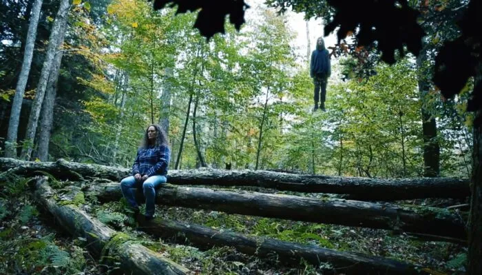 A woman in the forest with her daughter's floating ghost behind her