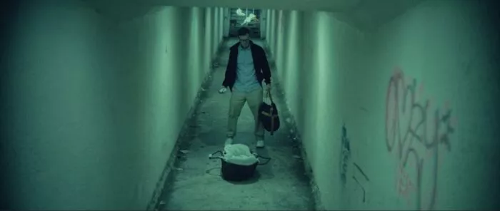 A man in long corridor holds a duffel bag while looking at at a baby carrier.