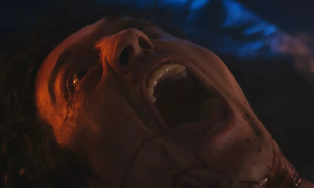 A man with blood coming from his mouth writhes in pain while laying on a tarp in BLEEDING