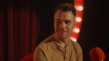 A smiling man on a stage with lights on either side of him