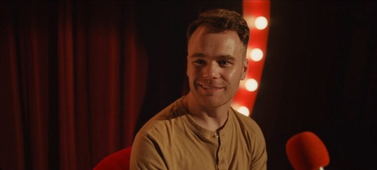 A smiling man on a stage with lights on either side of him