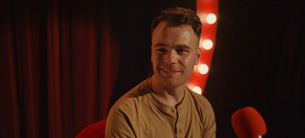 A smiling man on a stage with lights on either side of him