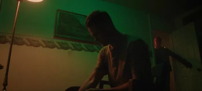 A man examines something unknown in his hands as a masked man enters the room in STARLIGHT