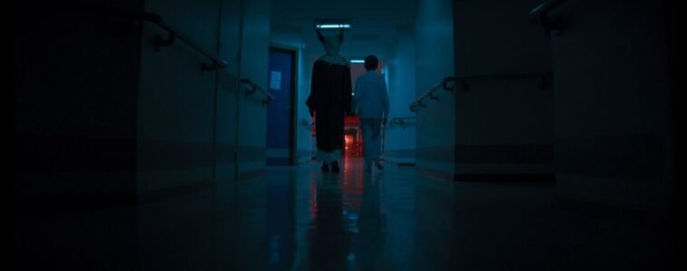 An antlered humanoid creature walks hand-in-hand with a young boy down a hospital corridor