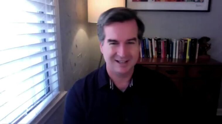 Warren Skeels smiles at a desk next to a window