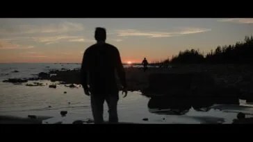 The shadow of a man in the foreground and another person in the background as the sun sets on a beach landscape in DADA.