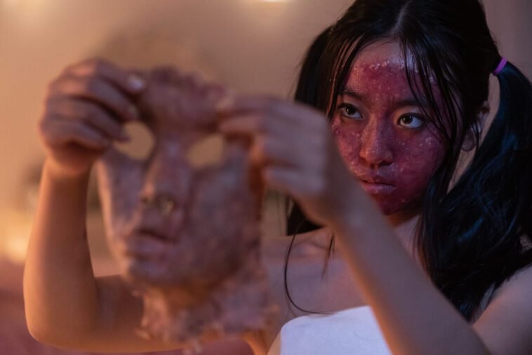A woman with a bloody face holds up the flesh of someone else's face in GRAFTED